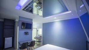 A modern hotel room with a skylight, a bed, a desk with two chairs, a small refrigerator, and a bathroom with a sink and mirror. - Drops Motel Campinas (Campinas)