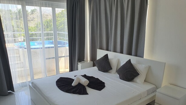 A modern bedroom with a large bed, white bedding, and a view of a swimming pool through large windows. - St. penthouse w/jacuzzi (Sosúa)
