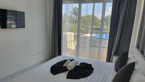 A hotel room with a bed, a flat-screen TV mounted on the wall, and a view of the outdoors through large windows. - St. penthouse w/jacuzzi (Sosúa)