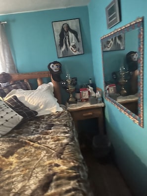 Une chambre à coucher avec un lit, une table de chevet, un miroir et un mur orné d’un tableau encadré.