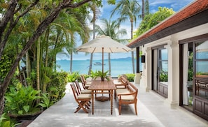 Relax in a serene outdoor seating area surrounded by lush tropical plants and palm trees, overlooking a calm sea.