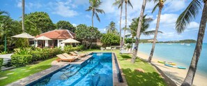Relax by the pool surrounded by lush greenery and palm trees, with the ocean view in the background.