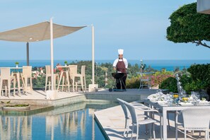A chef grilling outdoors with a pool and dining area in the background. - Baan Bon Khao - Choeng Mon (Koh Samui)