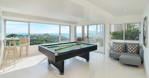 Enjoy expansive ocean views from the large windows in this serene living area, featuring a pool table and minimalist design.