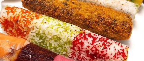 A variety of sushi rolls and a small dish of green sauce on a white plate.