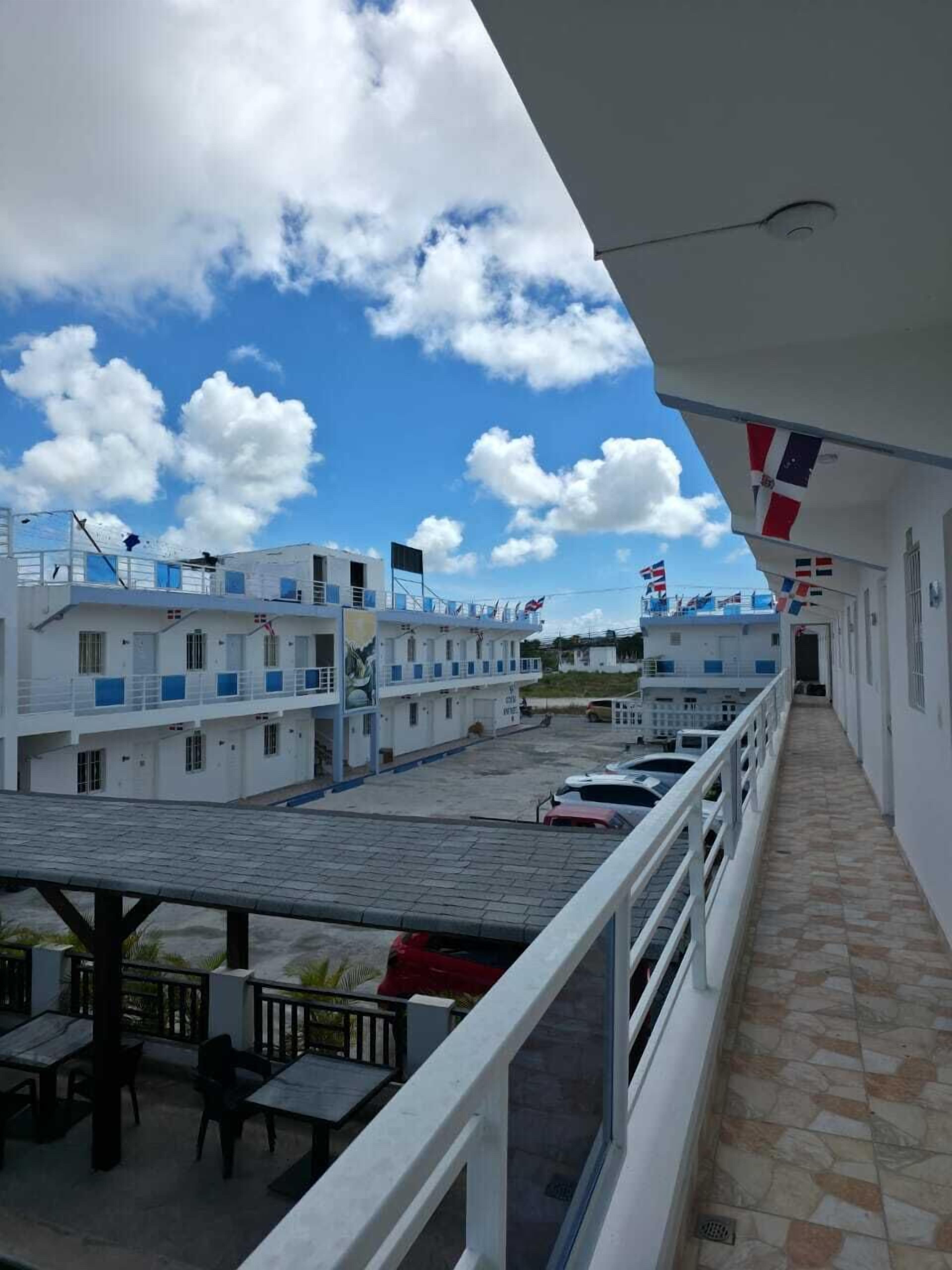A hotel with multiple white buildings, a covered outdoor area with tables and chairs, and flags.