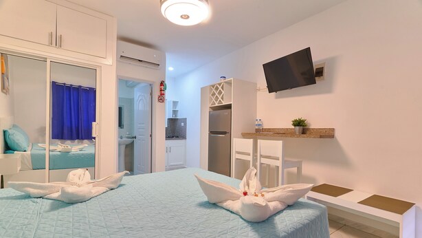Une chambre d’hôtel équipée d’un lit, d’un téléviseur fixé au mur, d’une petite table et d’un coin cuisine.