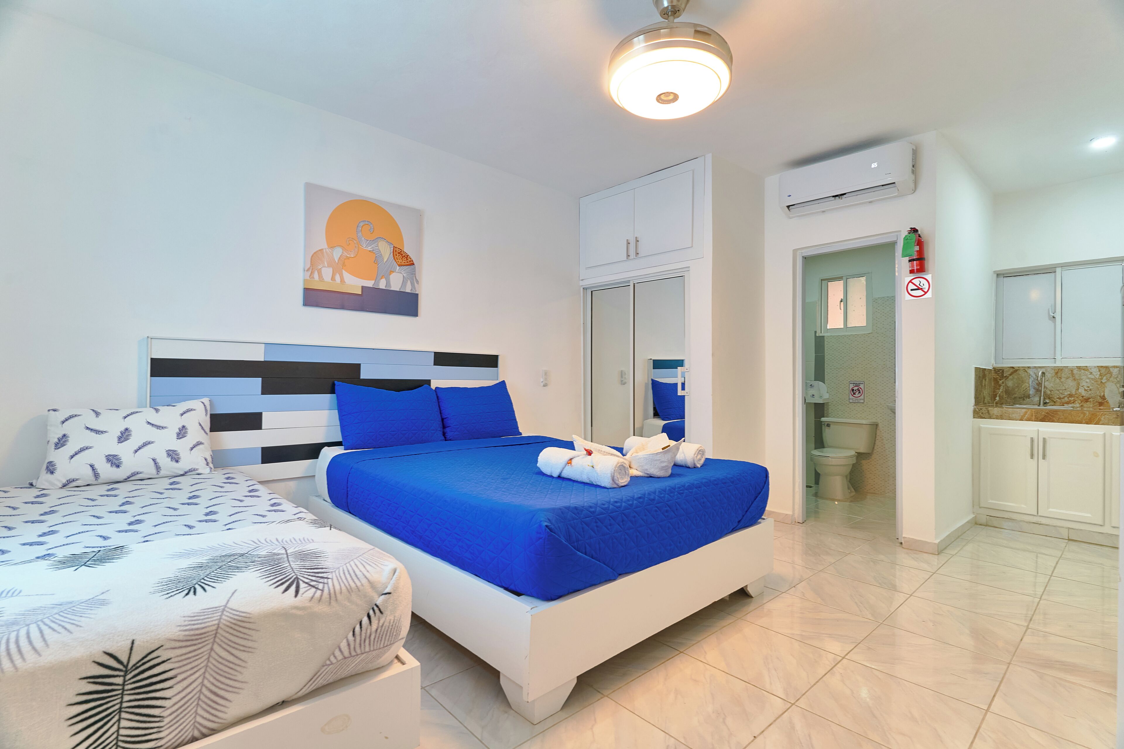 A hotel room with a large bed, a smaller bed, a bathroom, and an air conditioning unit.