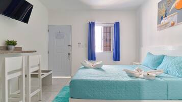 Un dormitorio ordenado con cama, escritorio, silla, televisor y ventana con cortinas.