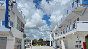 Un Costa Apart Hotel avec un ciel dégagé et quelques nuages, caractérisé par une structure à deux étages et plusieurs drapeaux.