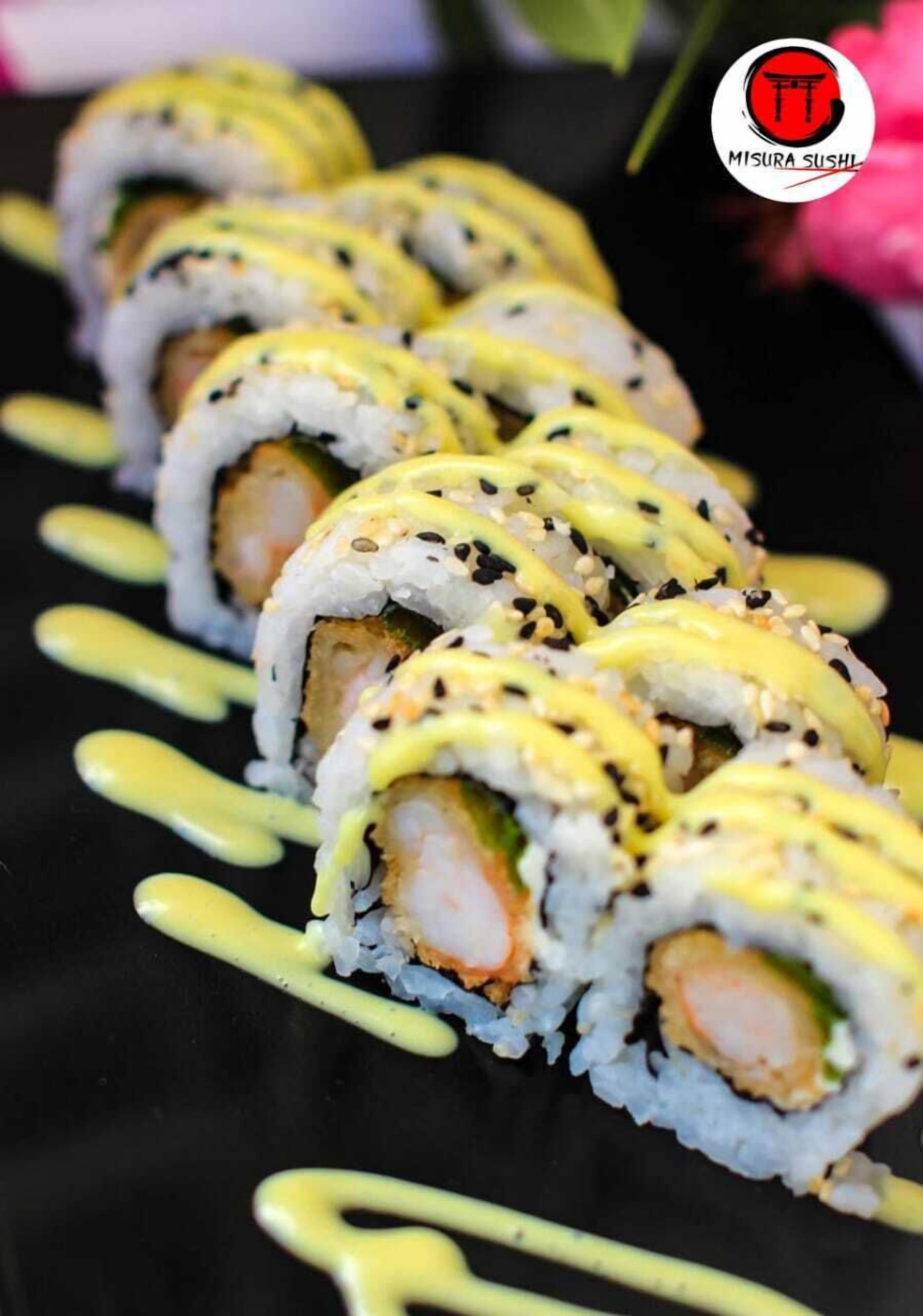 Uma fileira de sushis com molho amarelo sobre um prato preto.
