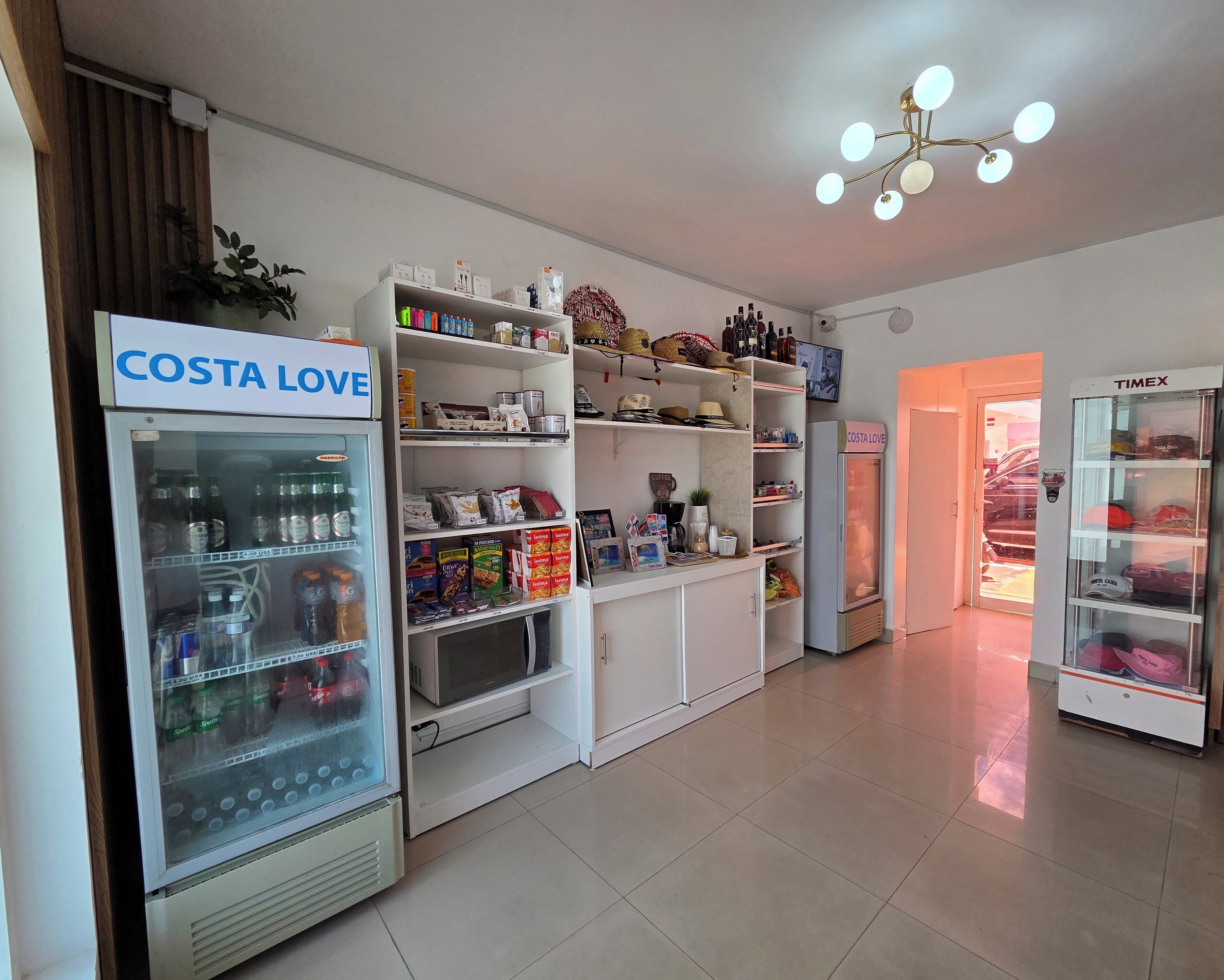 A hotel lobby with a Costa Love beverage machine, a Timex vending machine, and a variety of shelves stocked with snacks and toiletries.