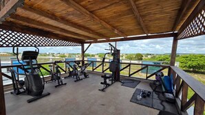Une salle de sport en plein air équipée de matériel d’exercice, dotée d’une terrasse en bois et offrant une vue sur un plan d’eau.