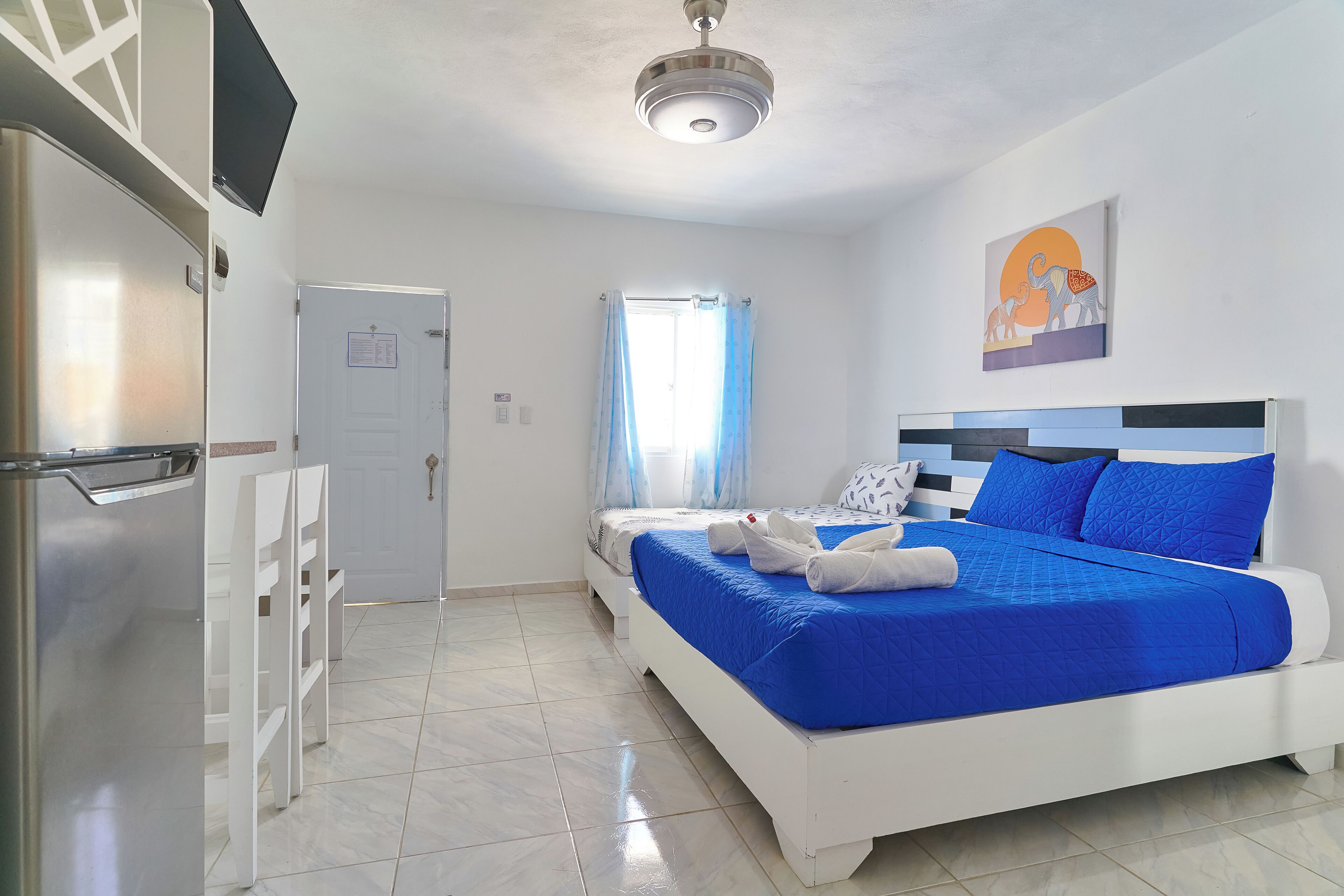 A hotel room with a bed, a desk, a chair, and a refrigerator.