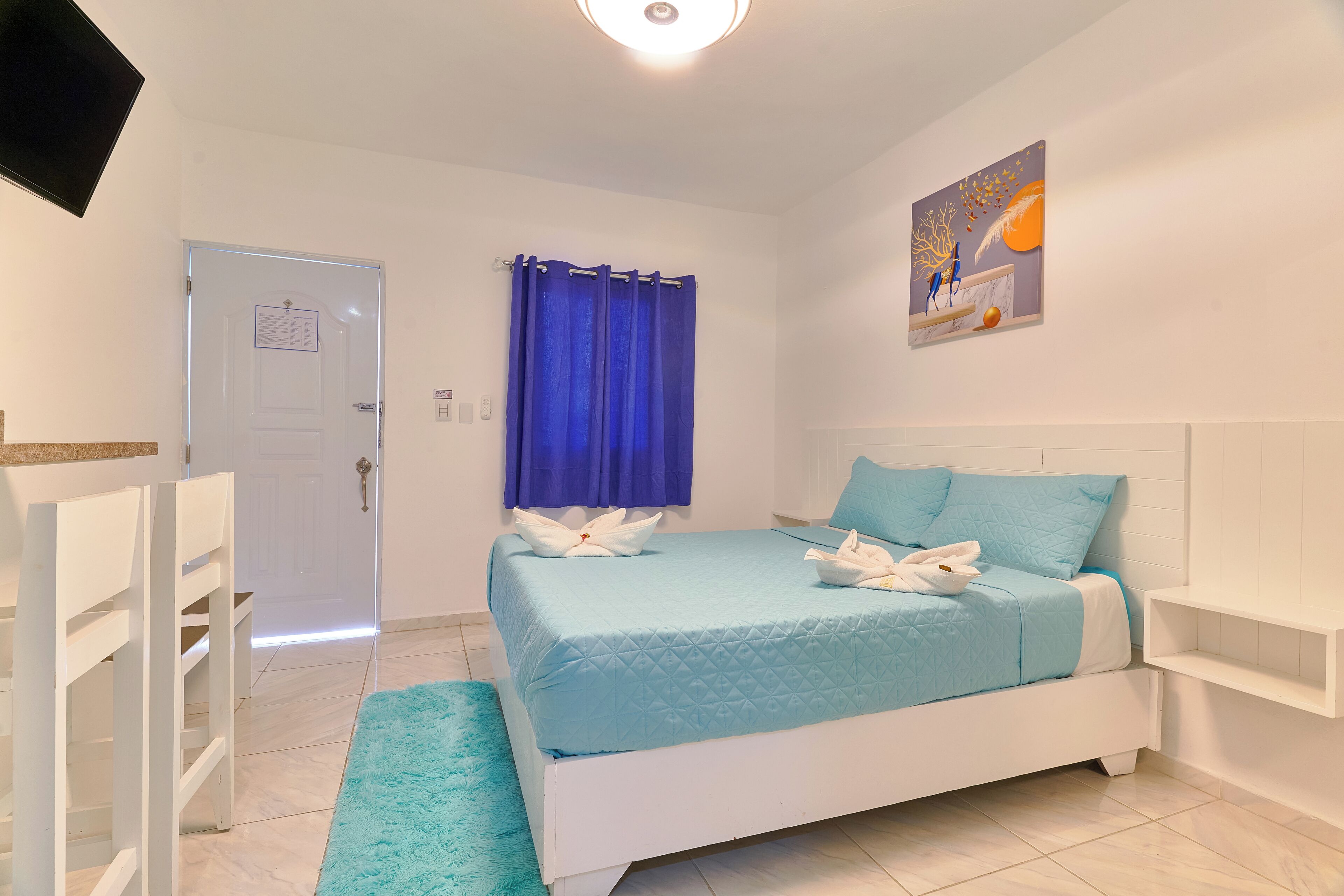 Quarto com cama, cortina azul, pintura e porta branca.