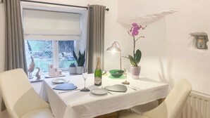 A dining table set for two with white chairs, a bottle of champagne, a green bowl, and a potted orchid. - 1 bedroom accommodation in Stainforth near Settle (Stainforth near Settle)