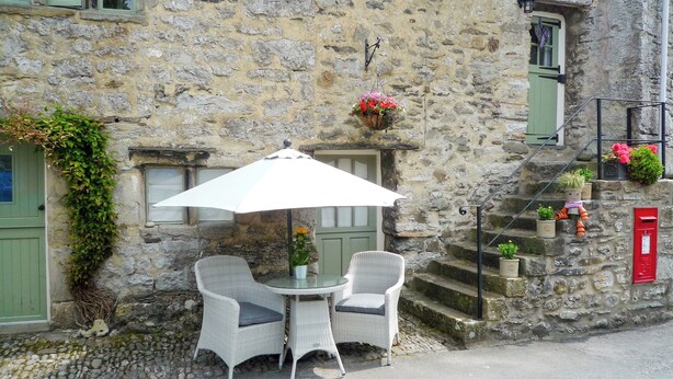 A stone building with a small outdoor seating area featuring two wicker chairs and a table under a white umbrella. - 1 bedroom accommodation in Stainforth near Settle (Stainforth near Settle)