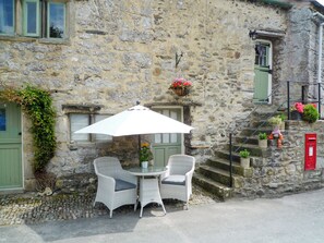 A stone building with a small outdoor seating area featuring two wicker chairs and a table under a white umbrella. - 1 bedroom accommodation in Stainforth near Settle (Stainforth near Settle)