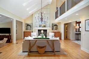 A spacious living area with a high ceiling, a chandelier, a central island with a green centerpiece, and a large window with a view. - Private Pool, Elevator, 4-Seater Golf Cart (fee), Golf Course view- 8 Hidden Green (Isle Of Palms)