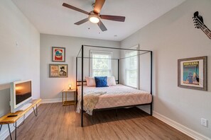 Un lit à baldaquin avec un cadre en bois, un ventilateur de plafond et un téléviseur posé sur un meuble en bois.