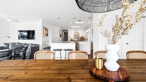 Una cocina moderna con armarios blancos, una isla central y una zona de comedor con mesa de madera y sillas de mimbre.