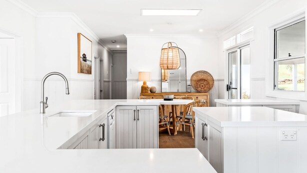 Una cocina moderna con armarios blancos, una isla central y un comedor con sillas de mimbre.