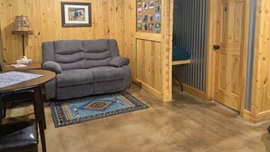 Ein gemütliches Zimmer mit einem grauen Sofa, einem kleinen Tisch mit Lampe und einem Teppich.