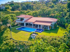 A large house with a swimming pool, surrounded by lush greenery and hills.