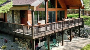 A cabin with a stone chimney, a wooden deck with outdoor seating, and a large glass door entrance. - Dog friendly, lakefront home perfect for families (Eagle River)