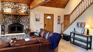 A cozy living room with a stone fireplace, a leather couch, and a wooden staircase. - Dog friendly, lakefront home perfect for families (Eagle River)