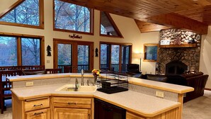 A spacious kitchen with a large island, wooden cabinets, and a stone fireplace. - Dog friendly, lakefront home perfect for families (Eagle River)