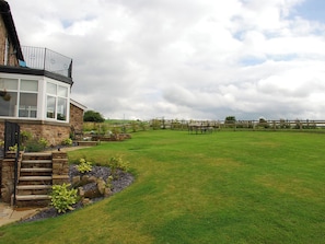 A stone house with a glass conservatory, a grassy yard, and a wooden fence.