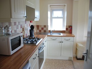 A compact kitchen with white cabinets, a microwave, a stove, a sink, and a window.