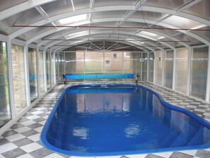 An indoor swimming pool with a checkered floor, glass walls, and a blue pool.