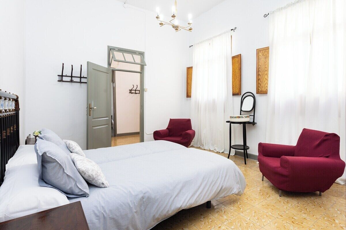 Une chambre à coucher avec un grand lit, deux fauteuils rouges, une petite table et un miroir.