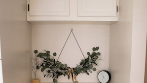 A white cabinet with two doors, a shelf with a clock, and a hanging plant. - Clyde's Cabin + Hot Tub (Carthage)