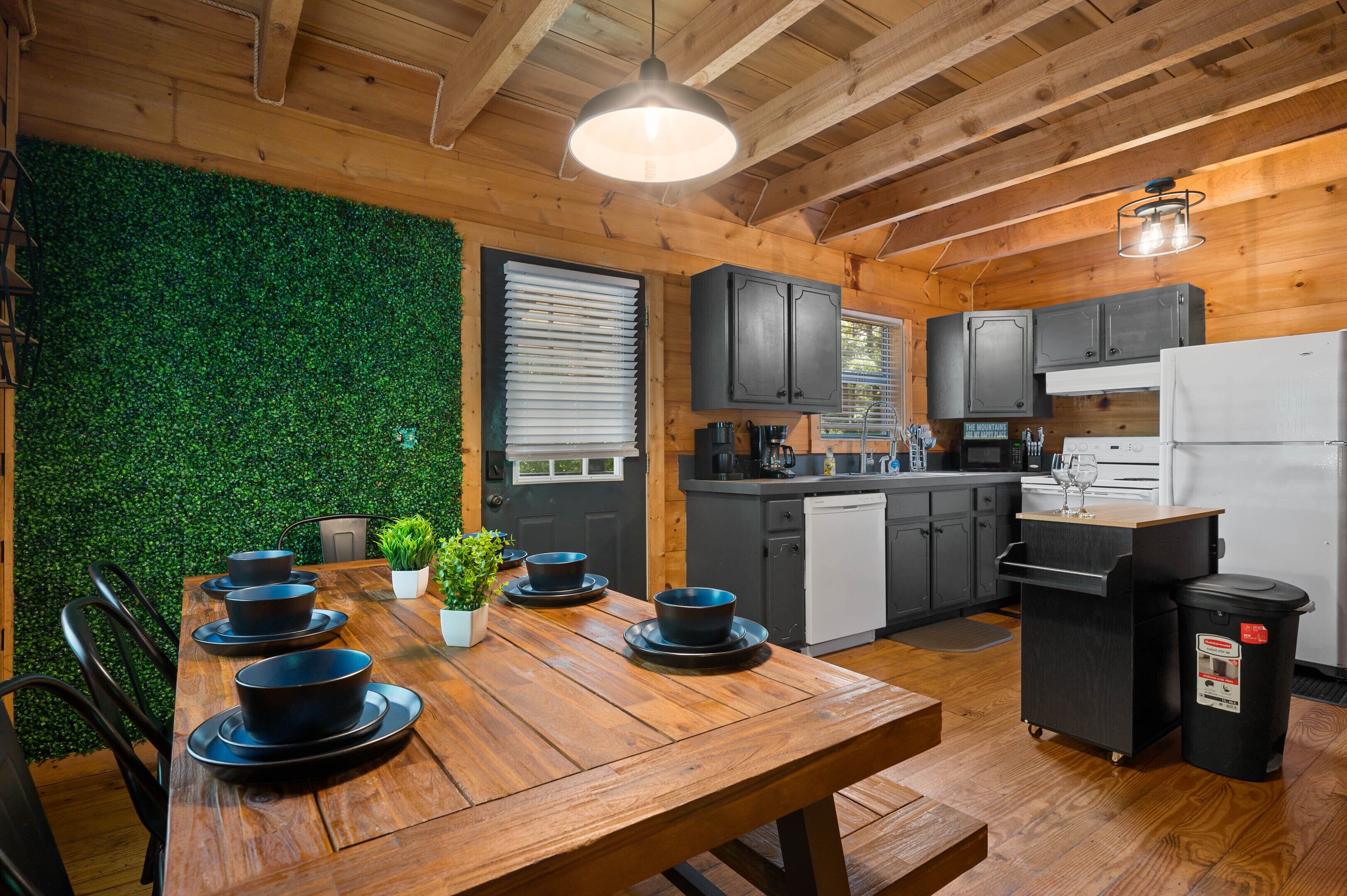 A wooden interior with a dining table set for four, a kitchen with grey cabinets, and a green wall.
