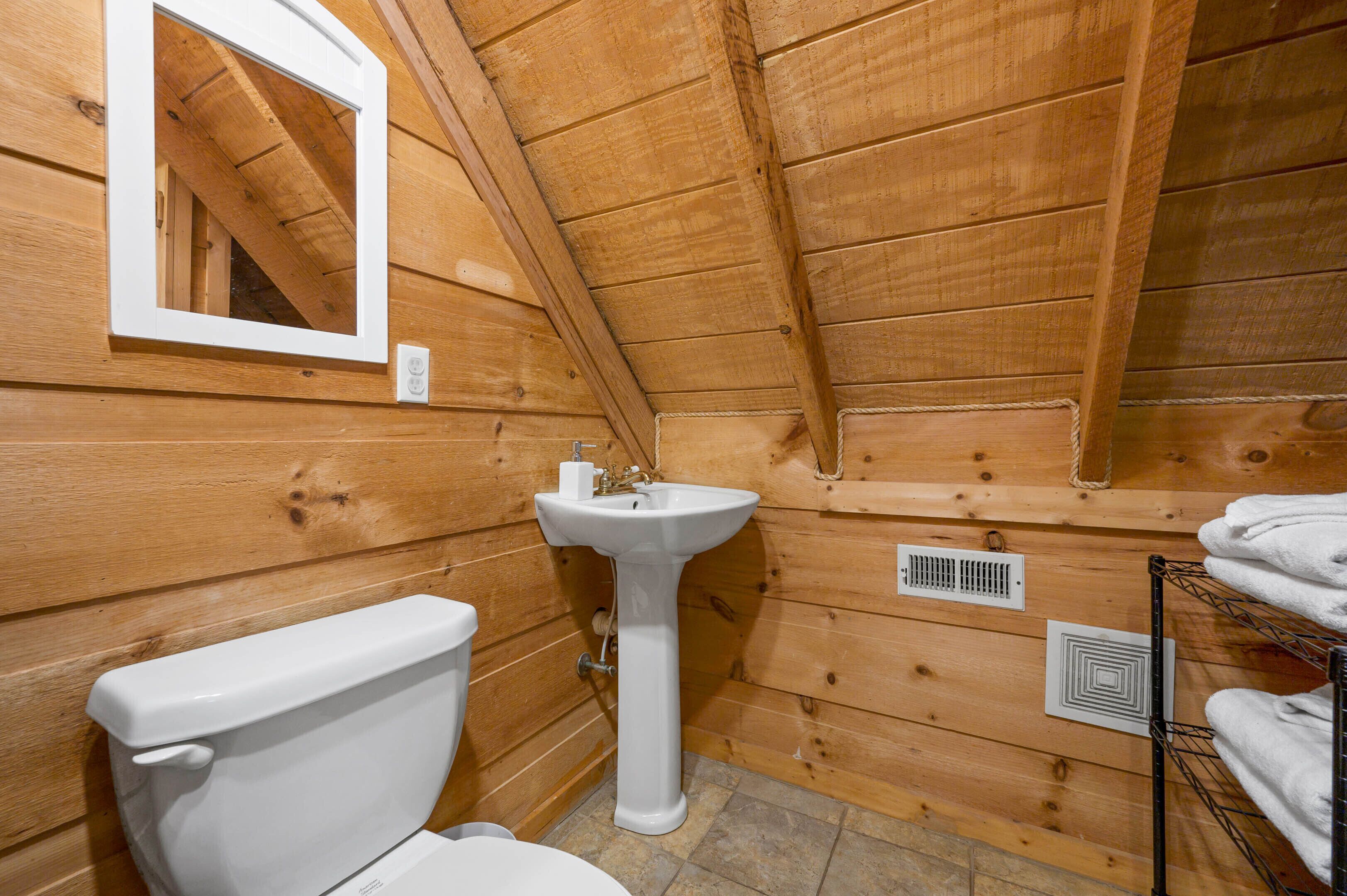 Un baño con paneles de madera, un inodoro blanco, un lavabo con pedestal y un perchero para toallas.