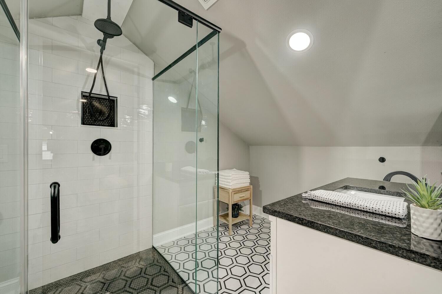 A modern bathroom with a glass-enclosed shower, a vanity with a granite countertop, and a hexagonal tile floor.