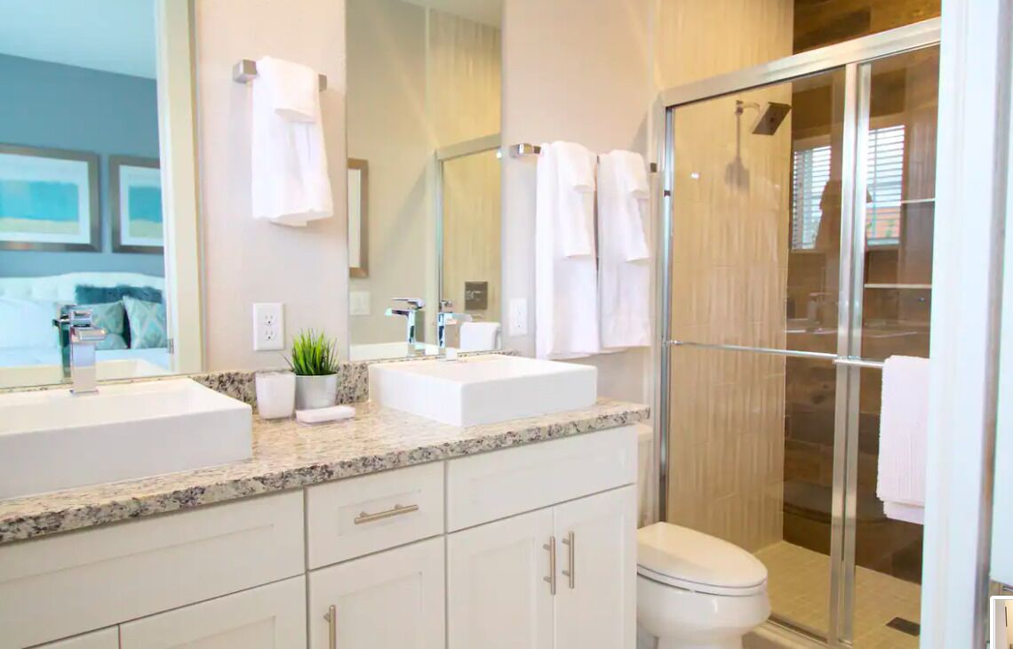 A modern bathroom with two sinks, a large mirror, and a glass shower enclosure.