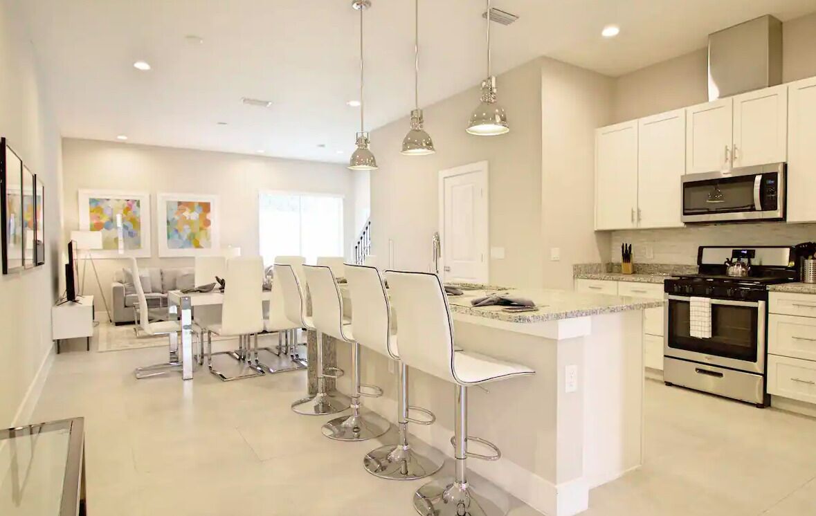 A modern kitchen with white cabinetry, stainless steel appliances, and a central island with bar stools.