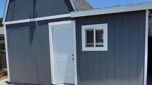 A gray shed with a white door and window, a metal ramp, and a clear sky. - Comfortable Tiny House in a Great Location (Moreno Valley)