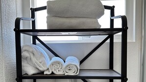 A black metal shelf unit with three shelves, holding rolled towels and a white container. - Comfortable Tiny House in a Great Location (Moreno Valley)