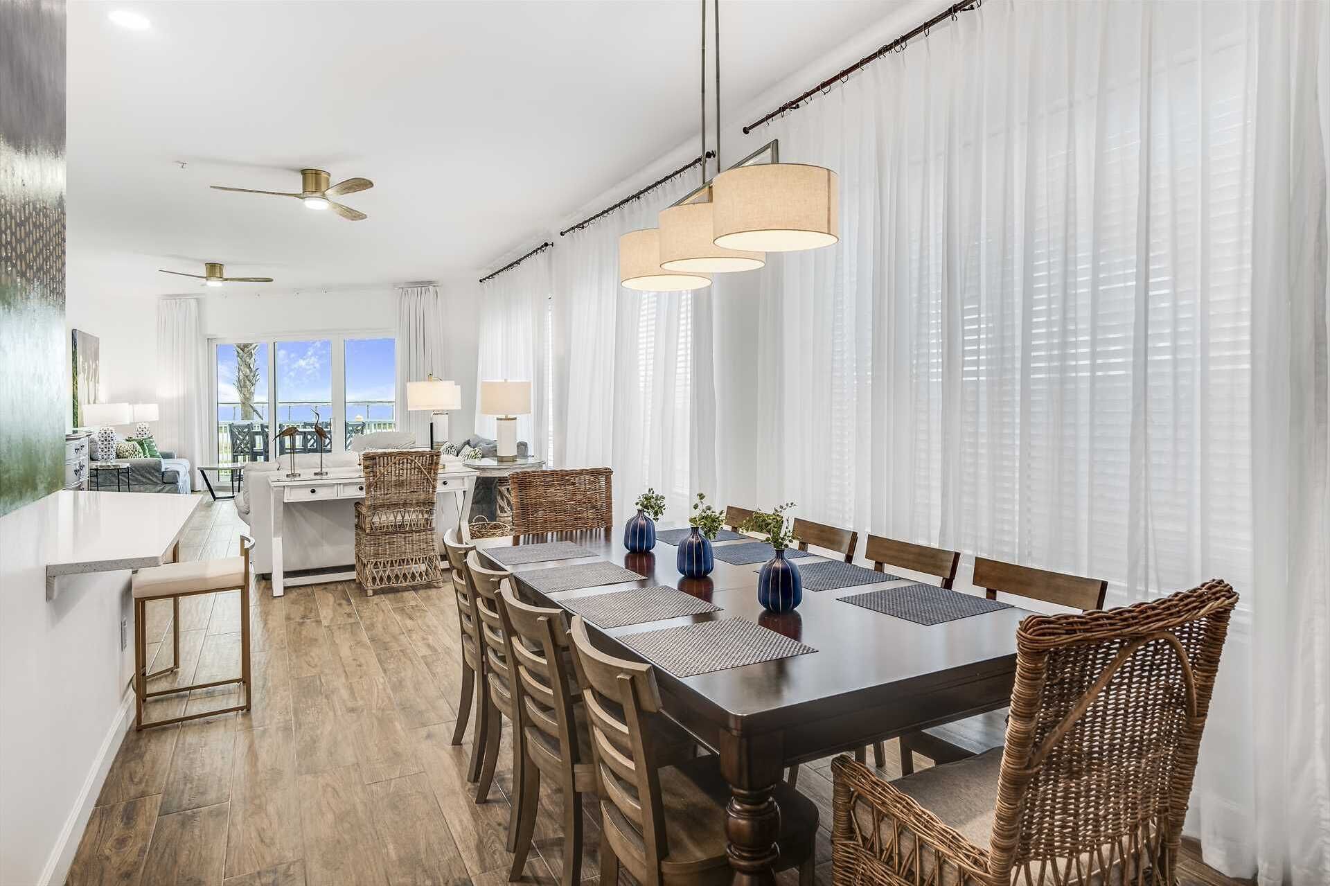 A modern dining area with a long table, wicker chairs, and pendant lighting.