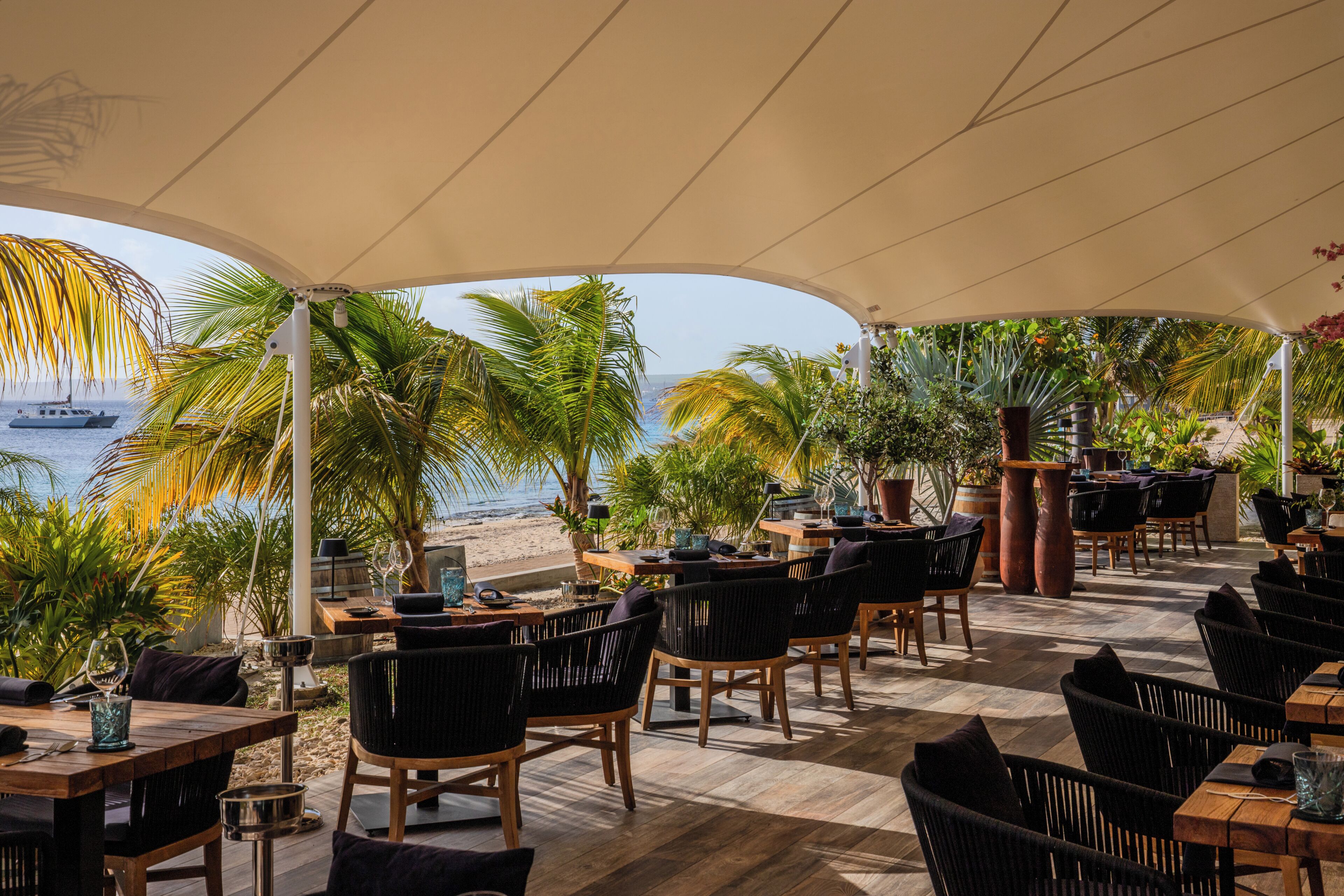 Een terras met tafels en stoelen, met uitzicht op een strand en de oceaan.