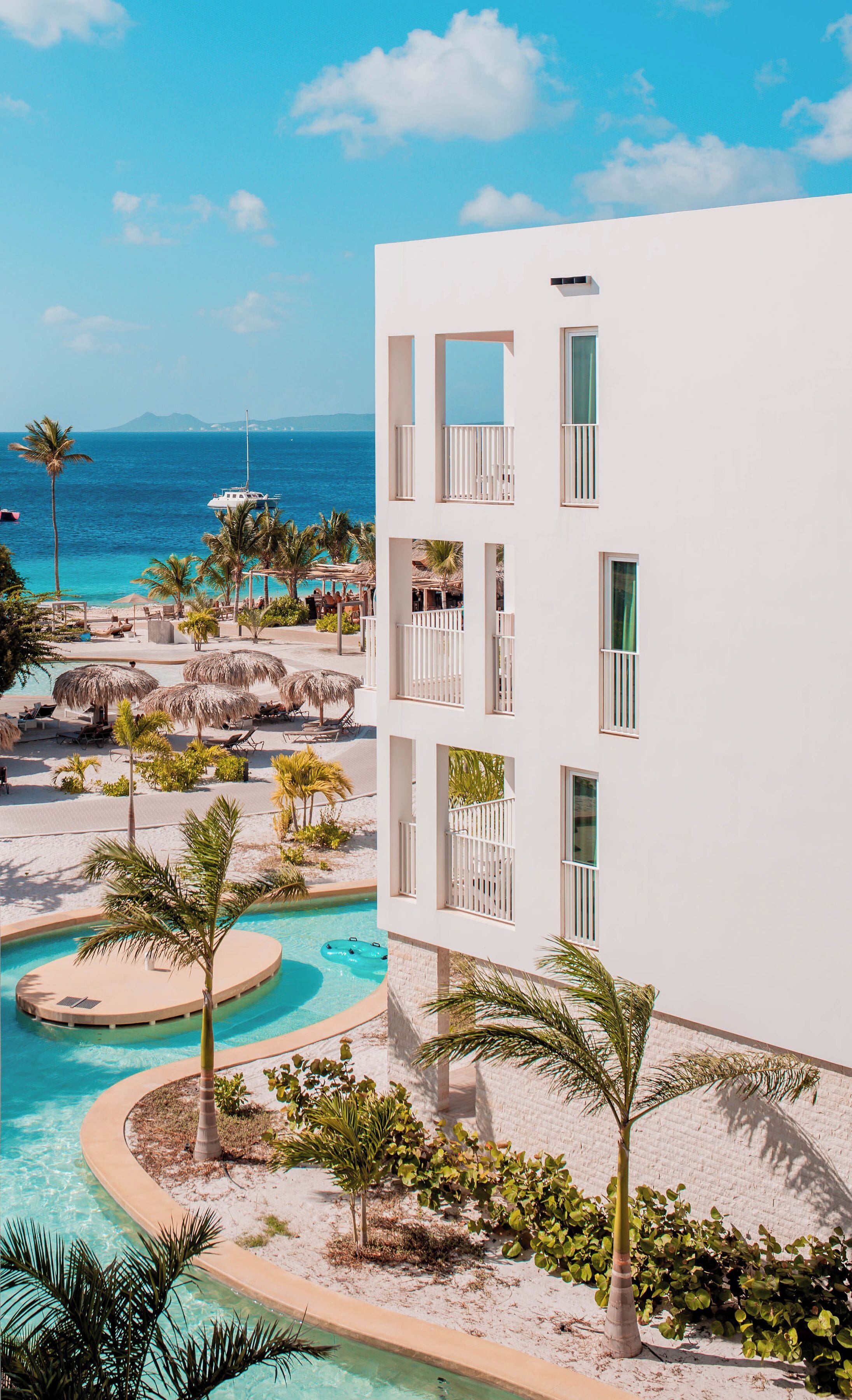 A resort with a pool, palm trees, and a view of the ocean.