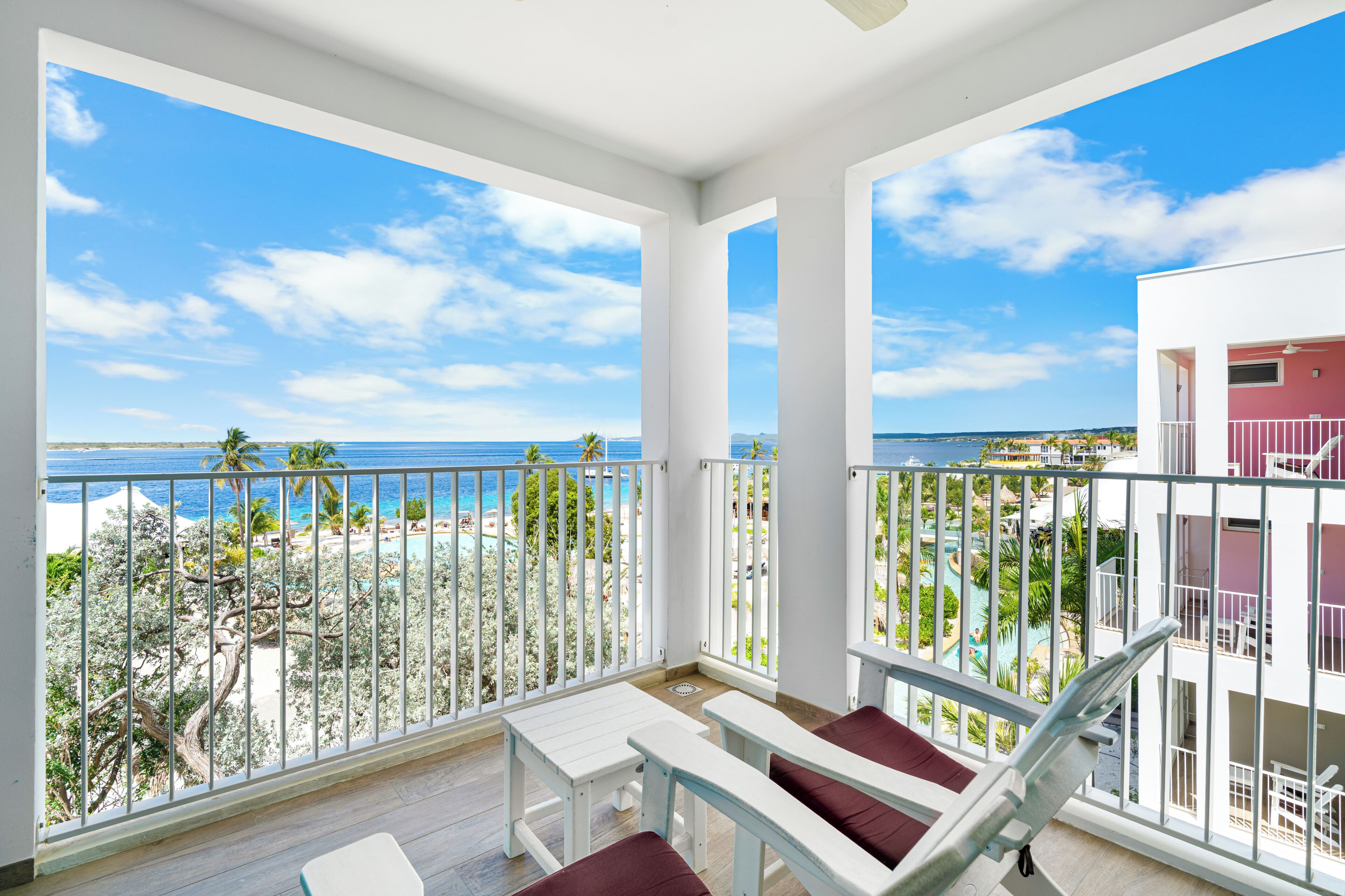 A balcony with white railings, white furniture, and a view of the beach and ocean.