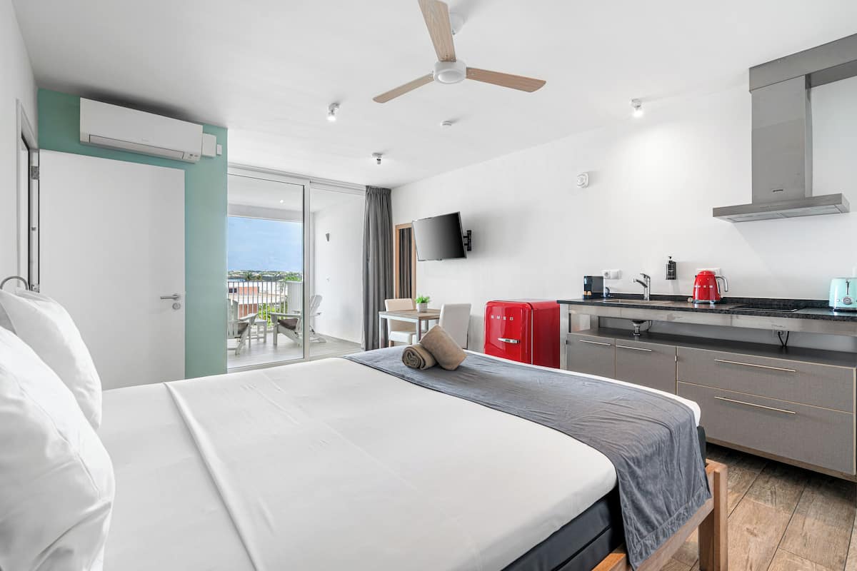 Une chambre d’hôtel moderne équipée d’un lit, d’une kitchenette, d’un ventilateur de plafond et offrant une vue sur l’extérieur.