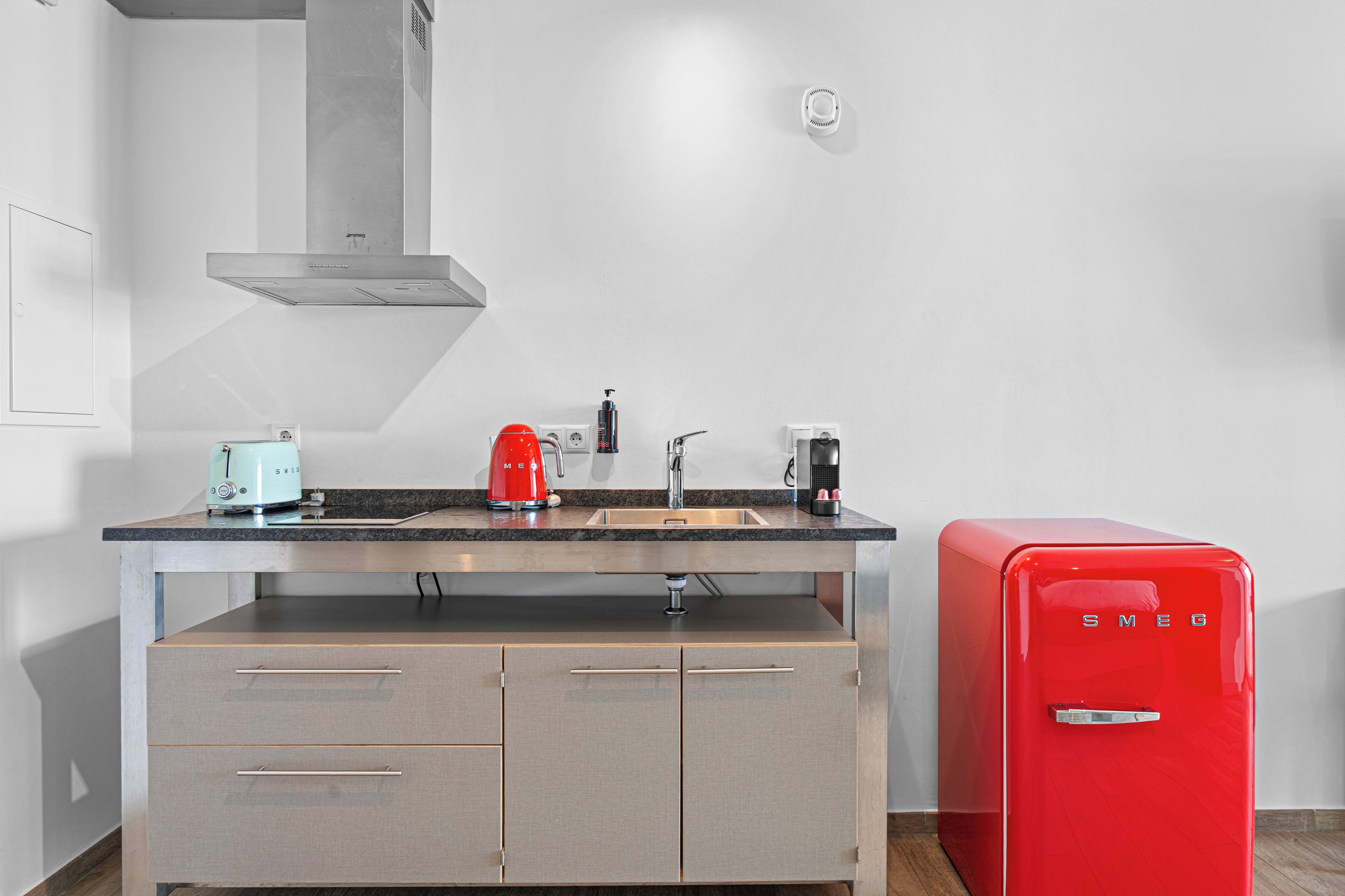 A modern kitchen with a stainless steel range hood, a red vintage-style refrigerator, and a countertop with a coffee maker and toaster.