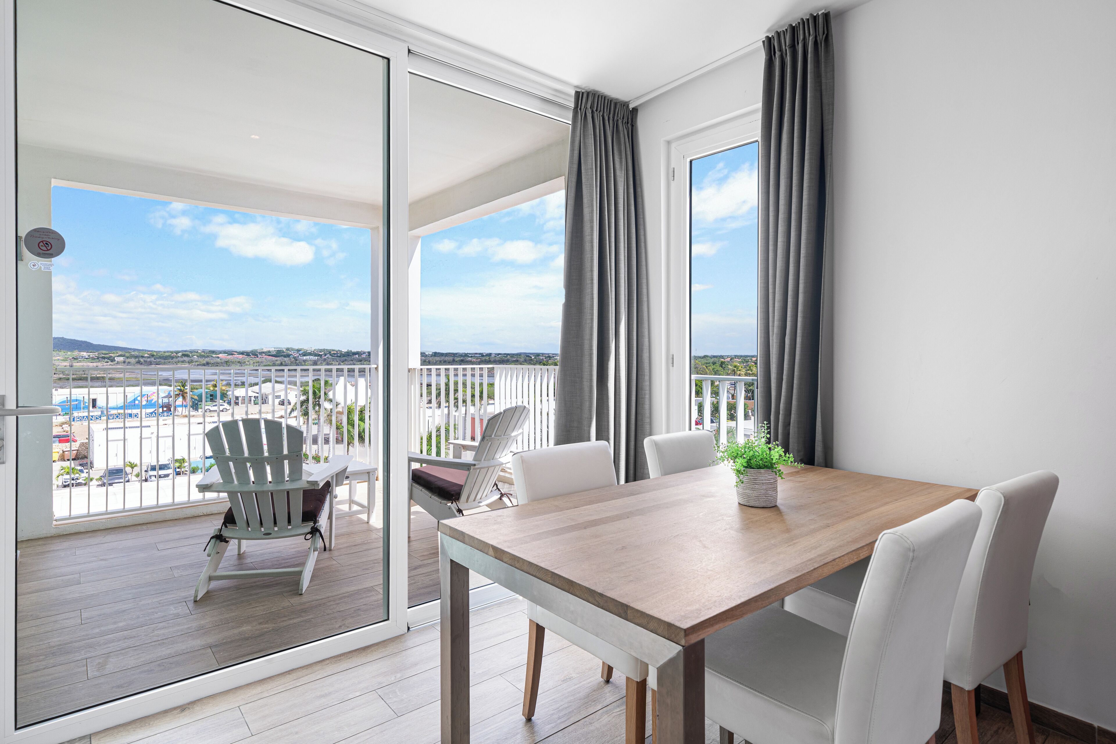 A balcony with a wooden table and chairs, a potted plant, and a view of the cityscape.